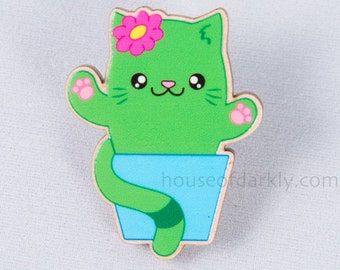 May include: A green cat-shaped cactus with a pink flower on top, wearing a blue pot with a green stripe. The cactus has a green tail and pink paws.