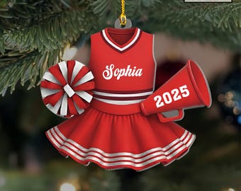 May include: A red and white cheerleader ornament with a matching pom-pom and megaphone. The ornament features a cheerleader uniform with the name "Sophia" and the year "2025" on the megaphone. The ornament is hanging from a gold string.