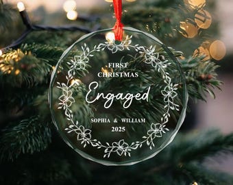 May include: Clear glass Christmas ornament with a red ribbon. The ornament has a floral wreath design and the words "First Christmas Engaged" with the names "Sophia & William" and the year "2025".