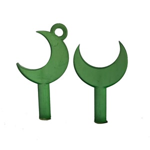 May include: Two green crescent moon-shaped objects. Each has a stem and a rounded top. One has a small loop at the top. The objects are made of a translucent material and are set against a white background.