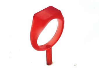 May include: A vibrant red ring with a rectangular top, set on a thin, matching stem. The ring's design is simple and modern, with a smooth, polished surface. The ring is likely a piece of jewelry or a fashion accessory.