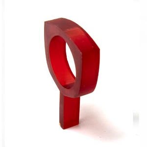 Peut inclure: Une bague rouge vif au design géométrique. La bague présente une bande rectangulaire qui se prolonge en une forme arrondie et ouverte. La bague est faite d'un matériau translucide, avec un design moderne et minimaliste.