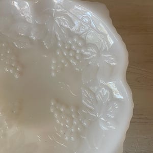 以下が含まれることがあります： ブドウの蔓のデザインが施された白いミルクガラスのボウル。ボウルは波状の縁があり、スナックやフルーツを盛り付けるのに最適です。