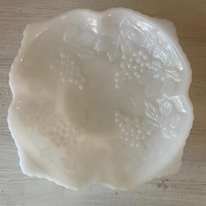 以下が含まれることがあります： ぶどうのデザインが施された白いミルクガラスのボウル。ボウルは波状の縁取りがされており、スナックやフルーツを盛り付けるのに最適です。