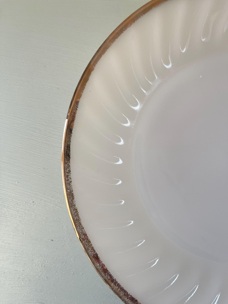 May include: A white ceramic plate with a gold rim. The plate has a rippled design.