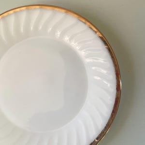 May include: White ceramic dinner plate with a gold rim and a swirl pattern.