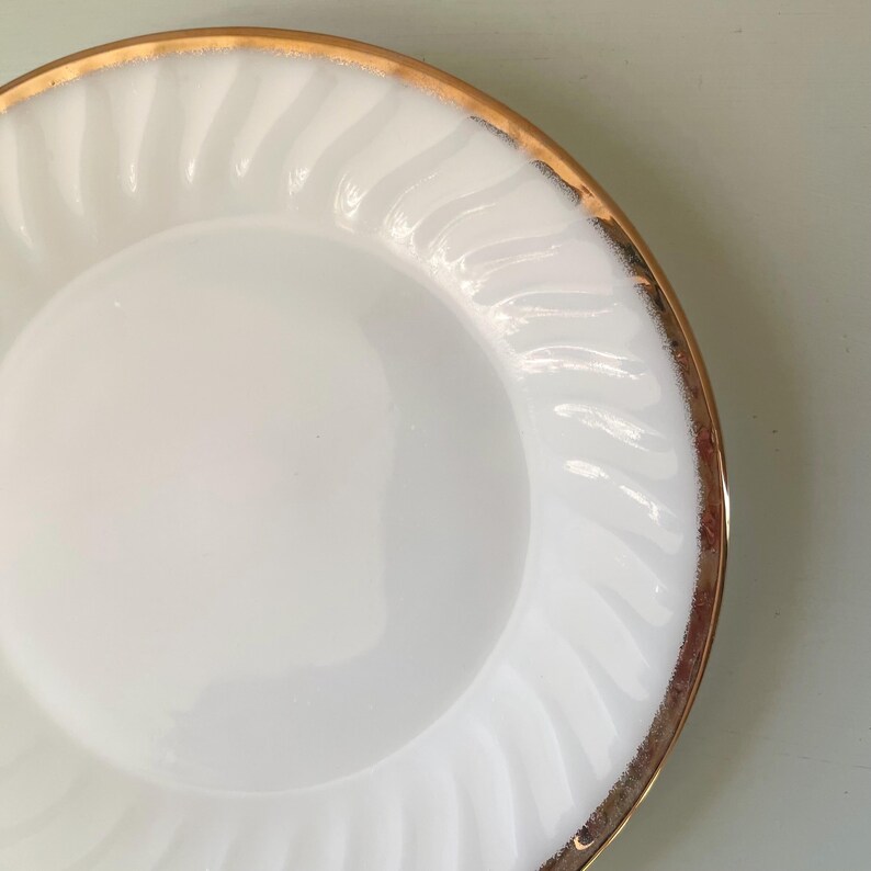 May include: White ceramic dinner plate with a gold rim and a swirl pattern.