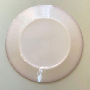 May include: The underside of a white ceramic plate with a pink rim. The plate has a small, circular mark in the centre that reads "Fire King USA".