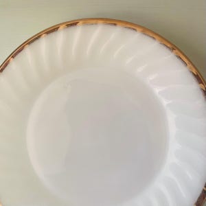 May include: White ceramic plate with a gold rim and a swirl design. The plate is empty.
