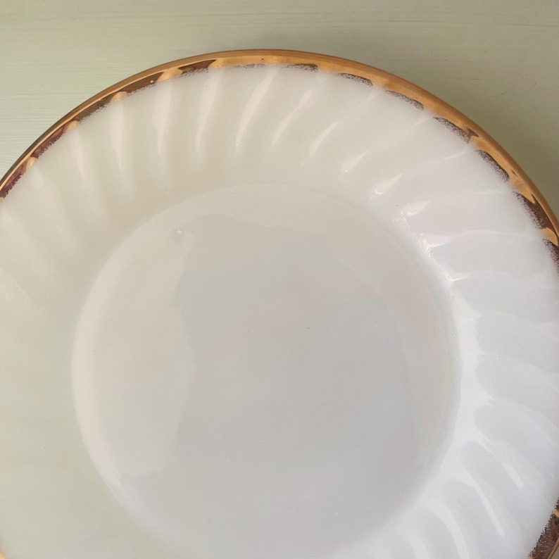 May include: White ceramic plate with a gold rim and a swirl design. The plate is empty.