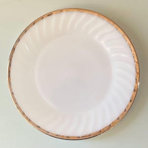 May include: A white milk glass dinner plate with a gold rim. The plate has a swirl design.