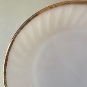 May include: White ceramic plate with a gold rim. The plate has a rippled texture.