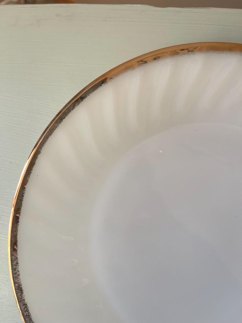 May include: White ceramic plate with a gold rim. The plate has a rippled texture.