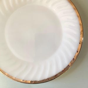 May include: White milk glass dinner plate with a gold rim. The plate has a swirl design.