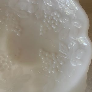 以下が含まれることがあります： ブドウの蔓のデザインが施された白いミルクガラスのボウル。ボウルは波状の縁があり、スナックやフルーツを盛り付けるのに最適です。