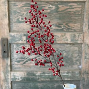 May include: A decorative artificial branch featuring numerous small, glossy red berries attached to thin, dark brown stems. The branch is arranged in a vertical, branching structure, showcasing a dense cluster of round red berries throughout.