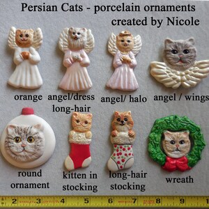 May include: A collection of porcelain ornaments featuring Persian cats. The ornaments include angel cats, a round ornament, a kitten in a stocking, a long-hair cat in a stocking, and a cat in a wreath. Measurements are in inches.