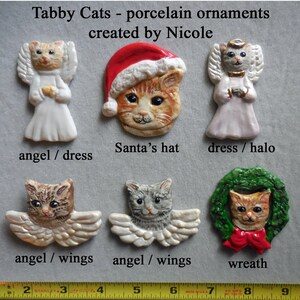 May include: A collection of porcelain tabby cat ornaments. The ornaments include a cat wearing a Santa hat, a cat with angel wings, and a cat in a wreath. The text on the image reads "Tabby Cats - porcelain ornaments created by Nicole."
