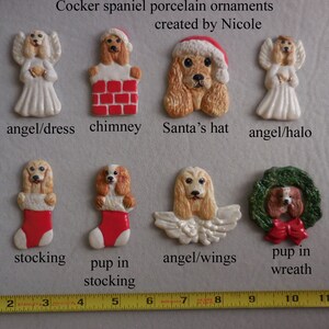 May include: A collection of Cocker spaniel porcelain ornaments. The ornaments include a dog in a Santa hat, a dog in a chimney, and dogs as angels. The ornaments are in various shapes and sizes, with a ruler in the foreground.