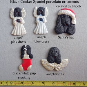 May include: A collection of black Cocker Spaniel porcelain ornaments. The ornaments include angel figures in white dresses, a dog wearing a Santa hat, a black and white dog in a red stocking, and a dog with angel wings. The text reads "Black Cocker Spaniel porcelain ornaments created by Nicole."
