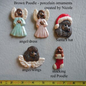 May include: A collection of brown poodle porcelain ornaments. The ornaments include poodle angels in dresses, a poodle wearing a Santa hat, a poodle with angel wings, and a poodle in a stocking. The text "Brown Poodle - porcelain ornaments created by Nicole" is visible.