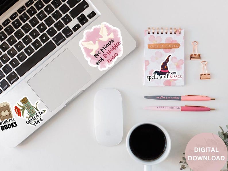 May include: A flat lay of a laptop with stickers on it. The stickers are pink and white and have text that says "buy me books", "cursed to read", "fae princes and forbidden kisses", and "spells and kisses". There is also a white mouse, a cup of coffee, two pens, and a small notebook with the text "keep it simple" on it.