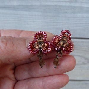 Puede incluir: Un par de pendientes de cuentas rojas con un diseño floral y detalles dorados.