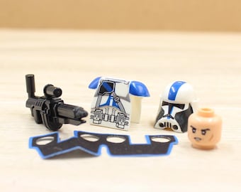 May include: A plastic toy construction figure set including a black blaster rifle, a white and blue torso piece with printed utility belt details, a white and blue helmet, a flesh-toned head piece, and a black fabric cape with blue trim.