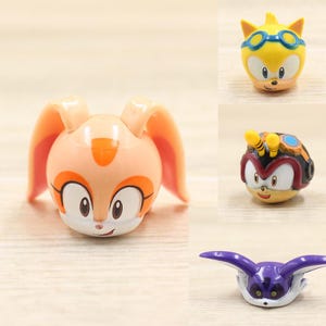 May include: Four small plastic figurines of characters from the Sonic the Hedgehog video game franchise. The characters are Cream the Rabbit, Jet the Hawk, Espio the Chameleon, and Vector the Crocodile. The figurines are all in their signature poses and colors.