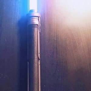 May include: A blue lightsaber with a black handle. The lightsaber is lit and the blade is glowing.