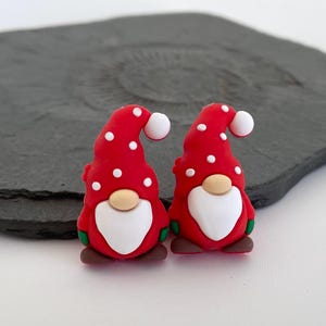 May include: Two festive gnome figurines. Each gnome has a red hat with white polka dots, a white beard, a tan nose, and brown shoes. The gnomes are small, likely for crafting or decoration.