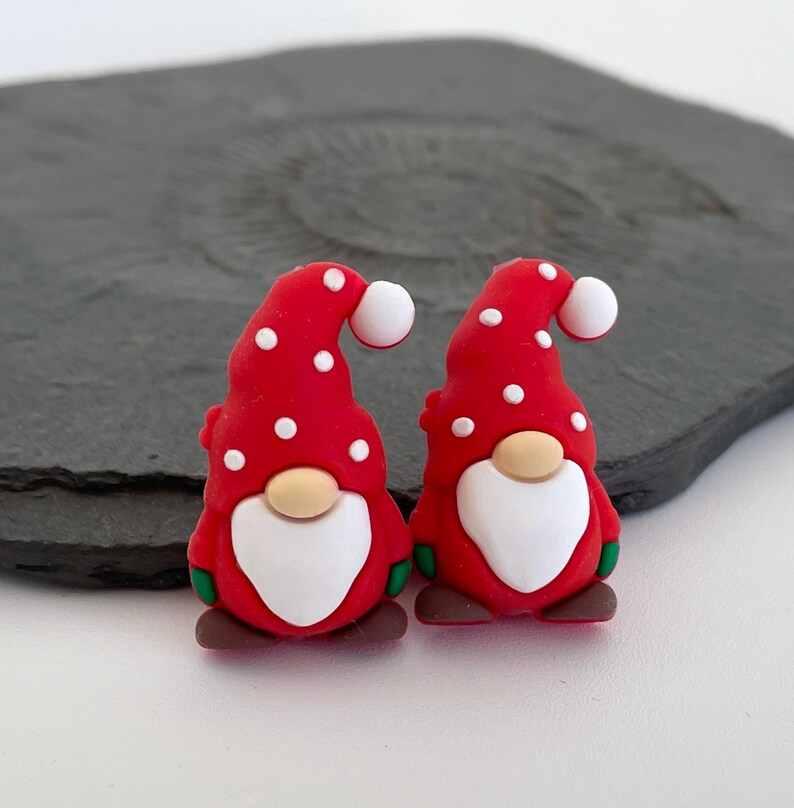 May include: Two festive gnome figurines. Each gnome has a red hat with white polka dots, a white beard, a tan nose, and brown shoes. The gnomes are small, likely for crafting or decoration.