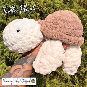 May include: A crocheted plush turtle toy with a white body and brown shell. The turtle has a black eye and is held in a hand.