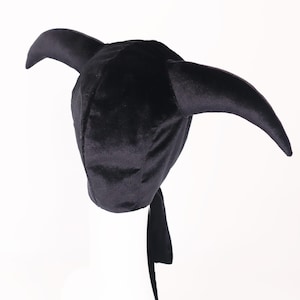May include: A black velvet hat with two curved horns and a long, flowing tail. The hat is designed in a unique style, perfect for costume parties or themed events. The hat is made of a soft, plush material.
