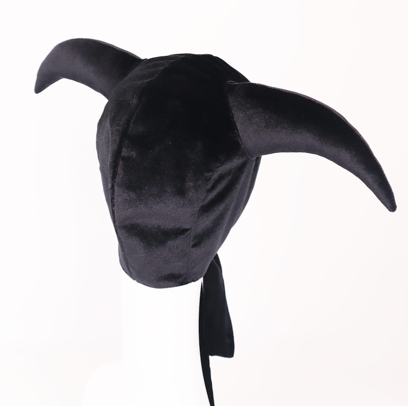 May include: A black velvet hat with two curved horns and a long, flowing tail. The hat is designed in a unique style, perfect for costume parties or themed events. The hat is made of a soft, plush material.