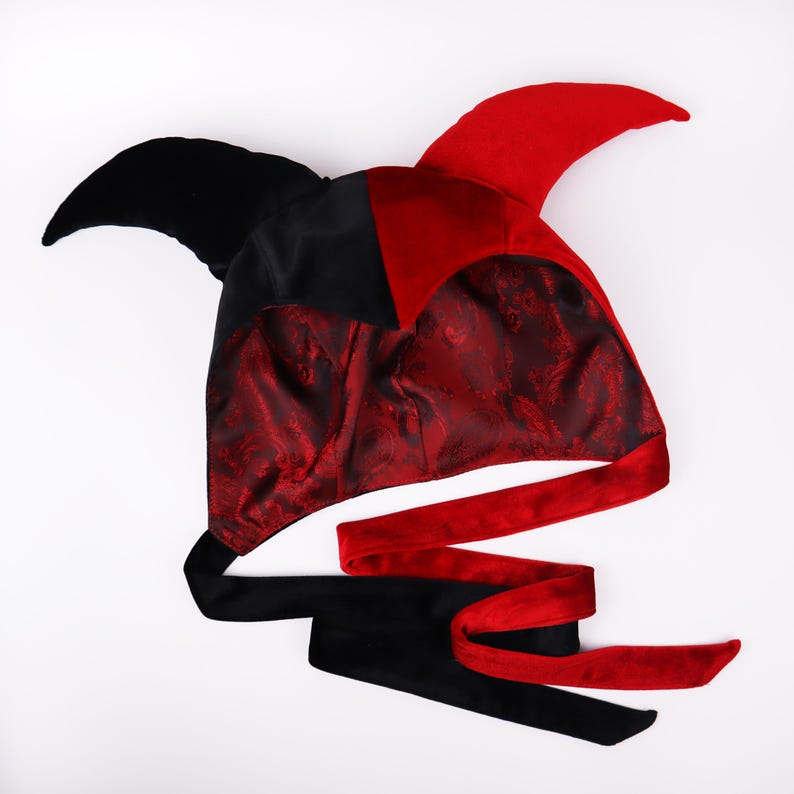 Pu&ograve; includere: Un cappello da giullare rosso e nero con una punta appuntita e un lungo nastro rosso e nero. Il cappello &egrave; in velluto e ha una fodera in raso.