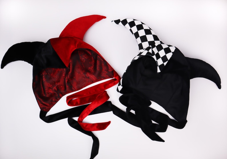 Pu&ograve; includere: Due cappelli da giullare in tessuto nero e rosso e tessuto a scacchi bianco e nero. Entrambi i cappelli hanno lunghe corna appuntite e lacci neri.