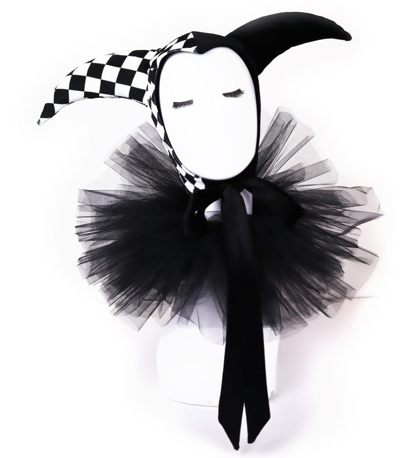 Pu&ograve; includere: Un cappello da giullare a scacchi bianco e nero con un colletto di tulle nero e un fiocco di velluto nero.