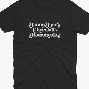 May include: Black t-shirt with the text "Danny Dyer's Chocolate Homunculus" in a white, retro font. The shirt has short sleeves and a crew neck. The design is centered on the chest.