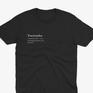 Puede incluir: Camiseta negra de cuello redondo con texto blanco. El texto dice "Tnetennba" con pronunciación fonética y definición: "Buenos días, eso es un buen Tnetennba". Una prenda informal.