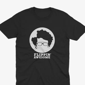 Könnte beinhalten: Ein schwarzes T-Shirt mit kurzen Ärmeln und einer weißen kreisförmigen Grafik auf der Brust. Die Grafik zeigt die schwarze Silhouette einer Person mit lockigem Haar und Brille über dem weißen Schriftzug FLIPPIN' AWESOME.