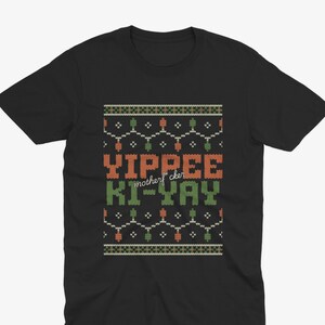 May include: Black t-shirt with a festive design. The design features the words "Yippee Ki-Yay motherf*cker" in orange and green, with a pattern of lights and decorative elements. The shirt is made of a soft material.