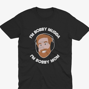May include: Black t-shirt with a white graphic of a man with a beard and headphones. The text "I'm Bobby Mudda I'm Bobby Mom" is printed on the shirt.