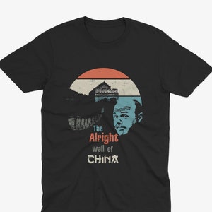 Peut inclure: Un t-shirt noir avec un graphique vintage de la Grande Muraille de Chine, un coucher de soleil et le visage d'un homme. Le texte "The Alright wall of CHINA" est imprimé sous le graphique.
