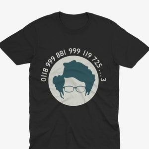 Könnte beinhalten: Schwarzes T-Shirt mit einer tealfarbenen Silhouette einer Person mit Brille in einem hellgrauen Kreis. Der Kreis ist von den weißen Zahlen 0118 999 881 999 119 725...3 umgeben. Das T-Shirt ist aus weichem Stoff.