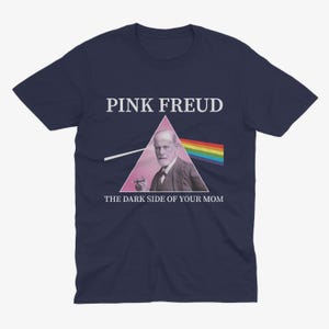 May include: Navy blue t-shirt with a pink triangle and a picture of Sigmund Freud. The text "PINK FREUD" is above the triangle and the text "THE DARK SIDE OF YOUR MOM" is below the triangle.
