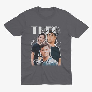 May include: A dark gray t-shirt with a white graphic print of three men. The text "Theo Von Gang Gang" is printed below the image.