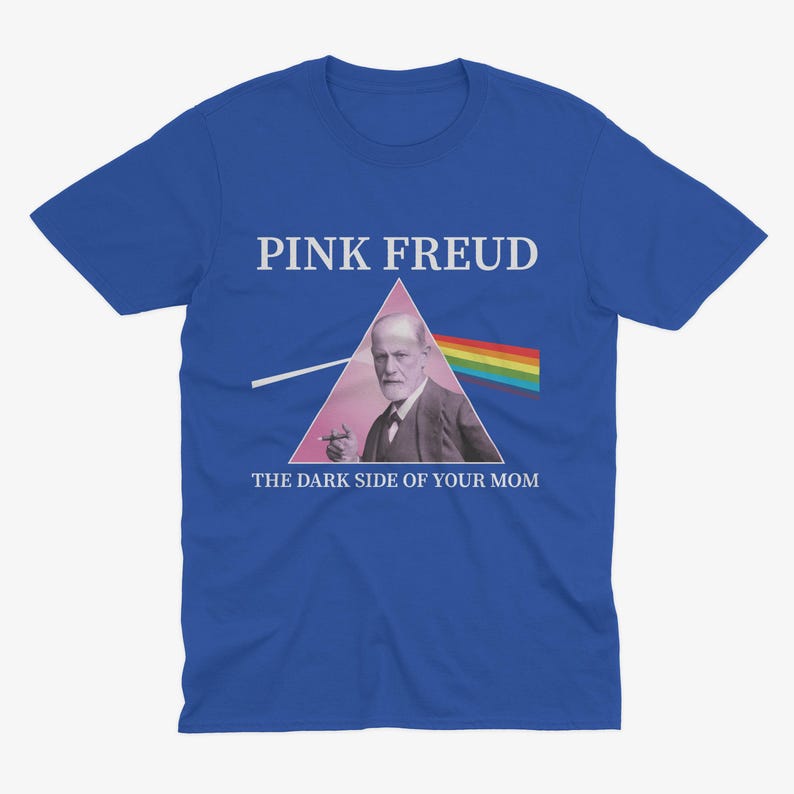 May include: A royal blue t-shirt with a white graphic of a pink triangle with a picture of Sigmund Freud inside. The text "PINK FREUD" is above the triangle and "THE DARK SIDE OF YOUR MOM" is below the triangle.