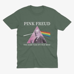 May include: A green t-shirt with a pink triangle and the text "PINK FREUD" above a picture of Sigmund Freud with a cigarette in his hand. The text below the image reads "THE DARK SIDE OF YOUR MOM".