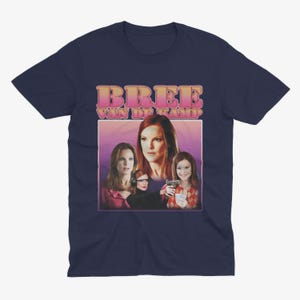 May include: Navy blue t-shirt with a retro-style graphic of Bree Van de Kamp from the TV show Desperate Housewives. The graphic features Bree and other characters from the show in a pink and purple background.